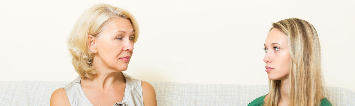 Mutter spricht mit eihrer erwachsenen Tochter auf dem Sofa, die Tochter hört still zu, eine feine Spannung im Raum sichtbar