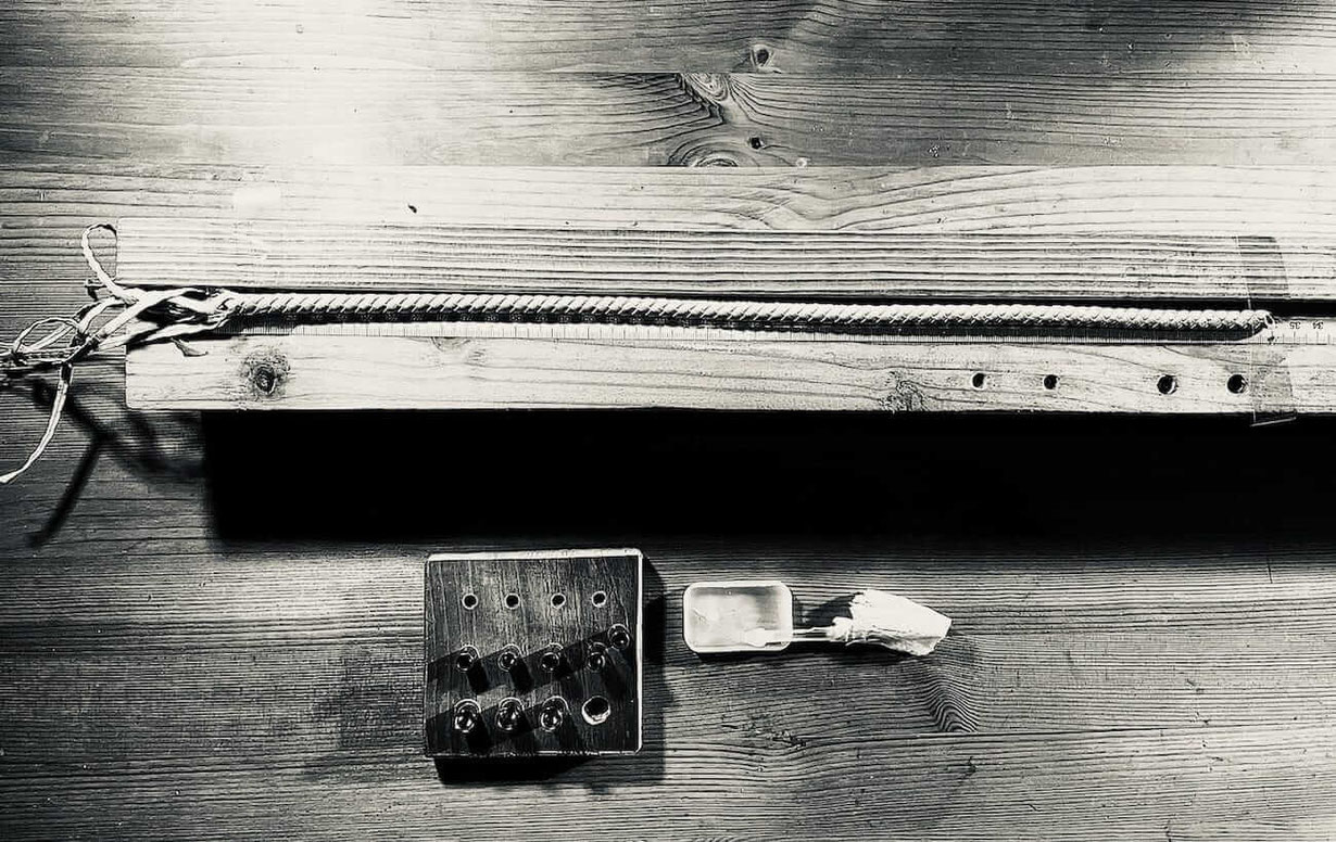 Ein geflochtenes Lederarmband noch ohne Verschlüsse eingespannt in eine Führung aus Holz um exakt die Länge abzuschneiden