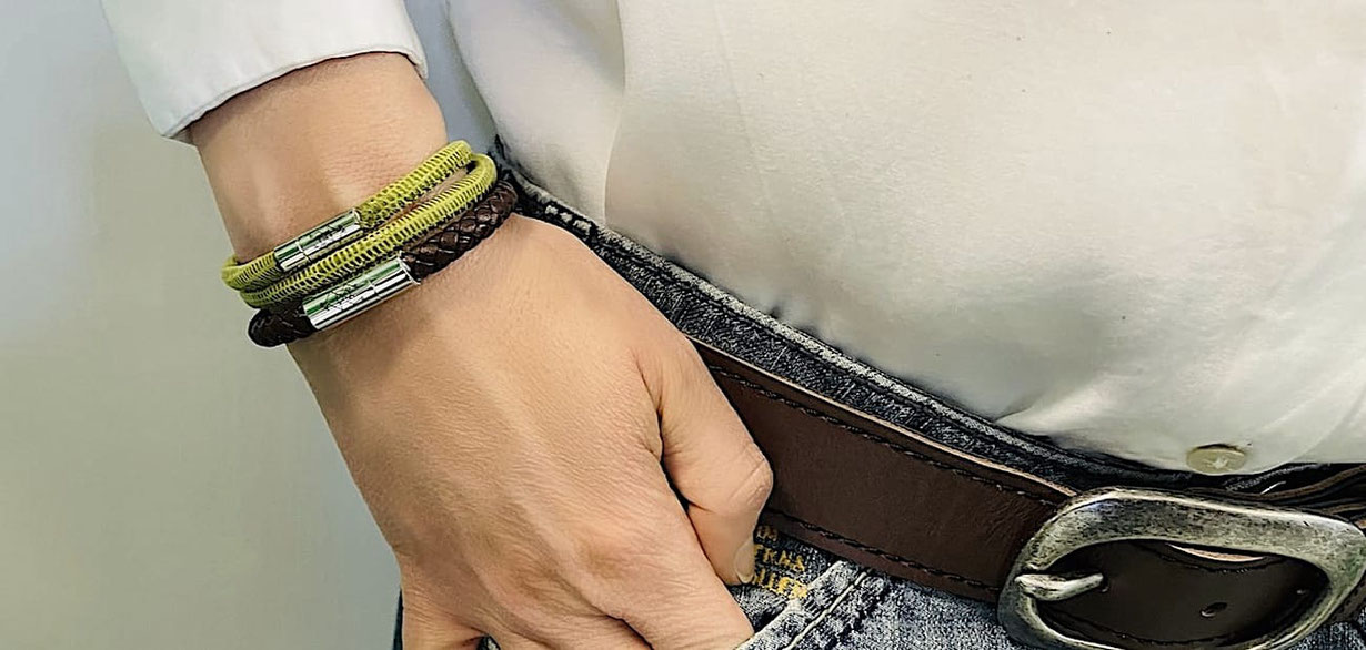 Rechtes Handgelenk einer Frau mit einem braunen geflochtenen Lederarmband in 8 mm Durchmesser und einem doppelt gewickelten Lederarmband aus grünem Leder mit Edelstahlverschluss