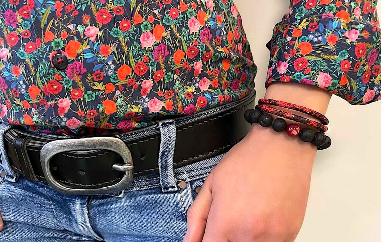 Eine Frau trägt am linken Handgelenk ein Perlenarmband aus schwarzen Lavaperlen mit roten Schmuckstein. Und darüber ein doppeltes rotes Lederarmband.