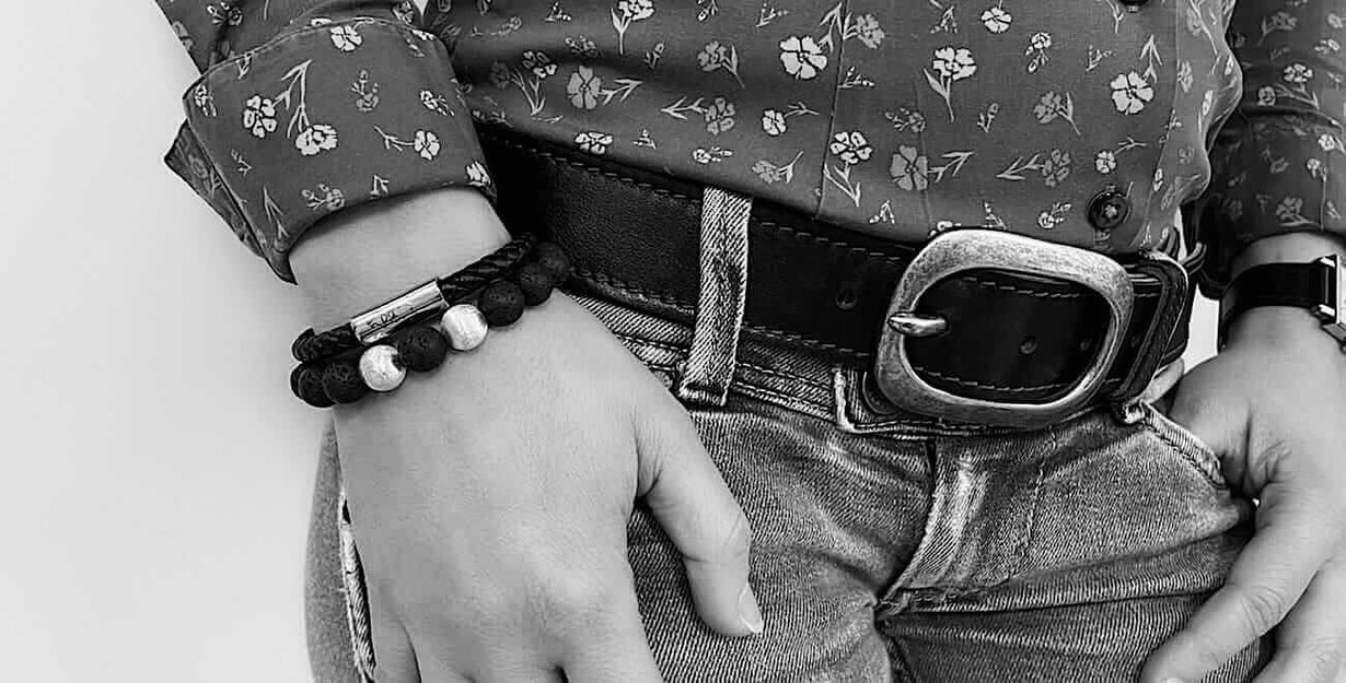 Schwarz/Weiß Foto mit dem rechten Handgelenk einer Frau mit einem schwarzen Lederarmband und einem schwarzen Lava Perlenarmband und zwei silbernen Perlen 