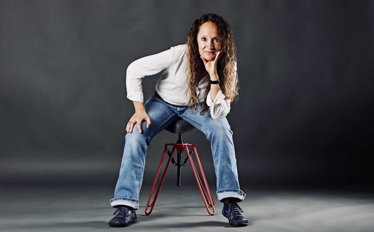 Frau in Jeans sitzt auf frontal auf dem leicht geneigten rotem Pendelhocker Poponaut. 