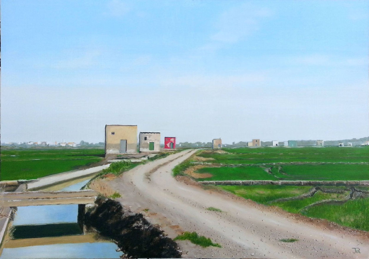 Casitas de Recatí junto a una acequia, camino rural, campos verdes y un pequeño puente de madera bajo cielo despejado.
