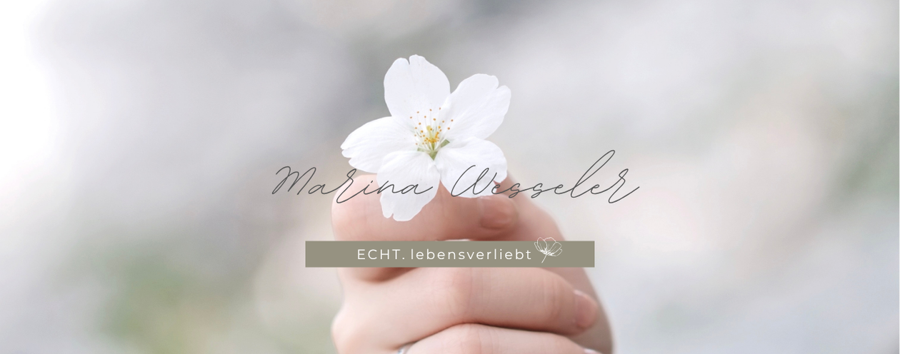 Minimalistisches Markenbild mit weißer Kirschblüte in einer Hand, ruhige grauweiße Farbwelt mit grünen Akzenten. Darstellung der Marke Echt lebensverliebt mit handschriftlichem Logo und florale.Gesundheit beginnt dort wo der Körper wieder Vertrauen fasst.
