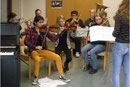 Schüler üben mit zwei Studentinnen ein Musikstück ein. 