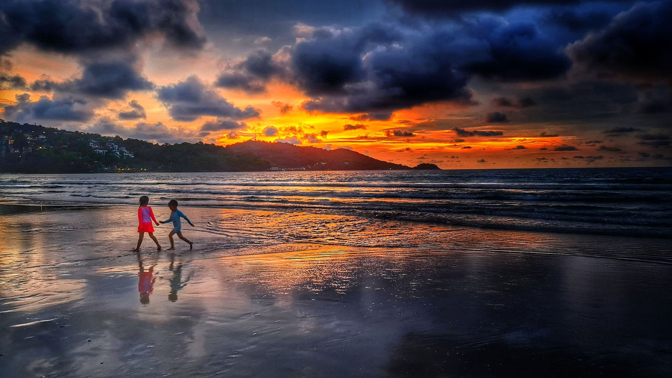 Kinder spielen bei Sonnenuntergang am Patong Beach, Phuket