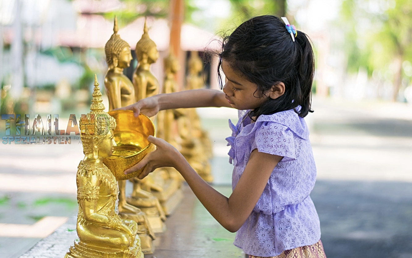 Mädchen schüttet Wasser über eine Buddhastatue, beim Songkran Festival in Thailand