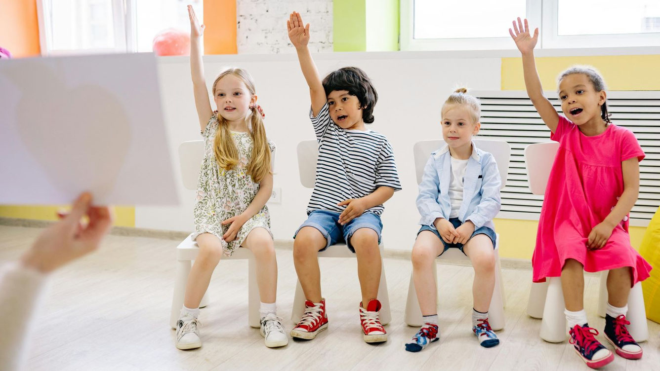 Kinder in einem Klassenzimmer mit erhobenen Händen als Symbol für die Entwicklung der Lernendenzahlen an der Volksschule im Kanton Luzern.