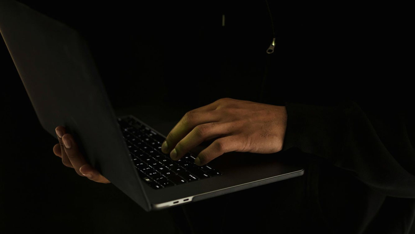 Hände einer Person tippen im Dunkeln auf einem Laptop, Symbolbild für Online-Radikalisierung, soziale Medien und algorithmische Filterblasen bei Jugendlichen.