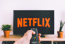 Hand met afstandbedining die naar tv wijst waarop Netflix te zien is