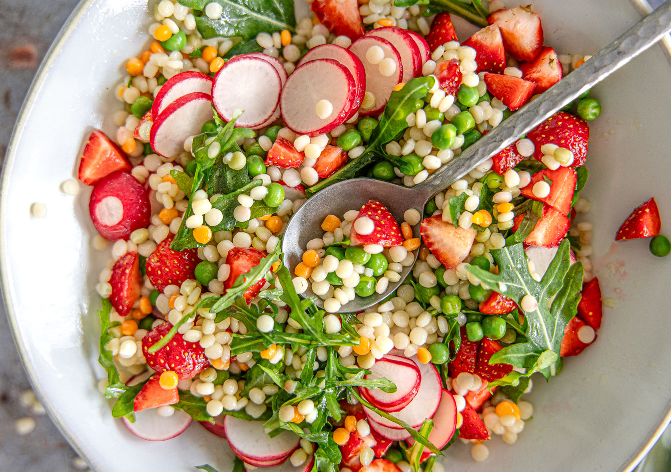Pearl Couscous Salat mit Erdbeeren, fein gehobelten Radieschen, Erbsen und Rucola in einer Schüssel – frisch und bunt angerichtet