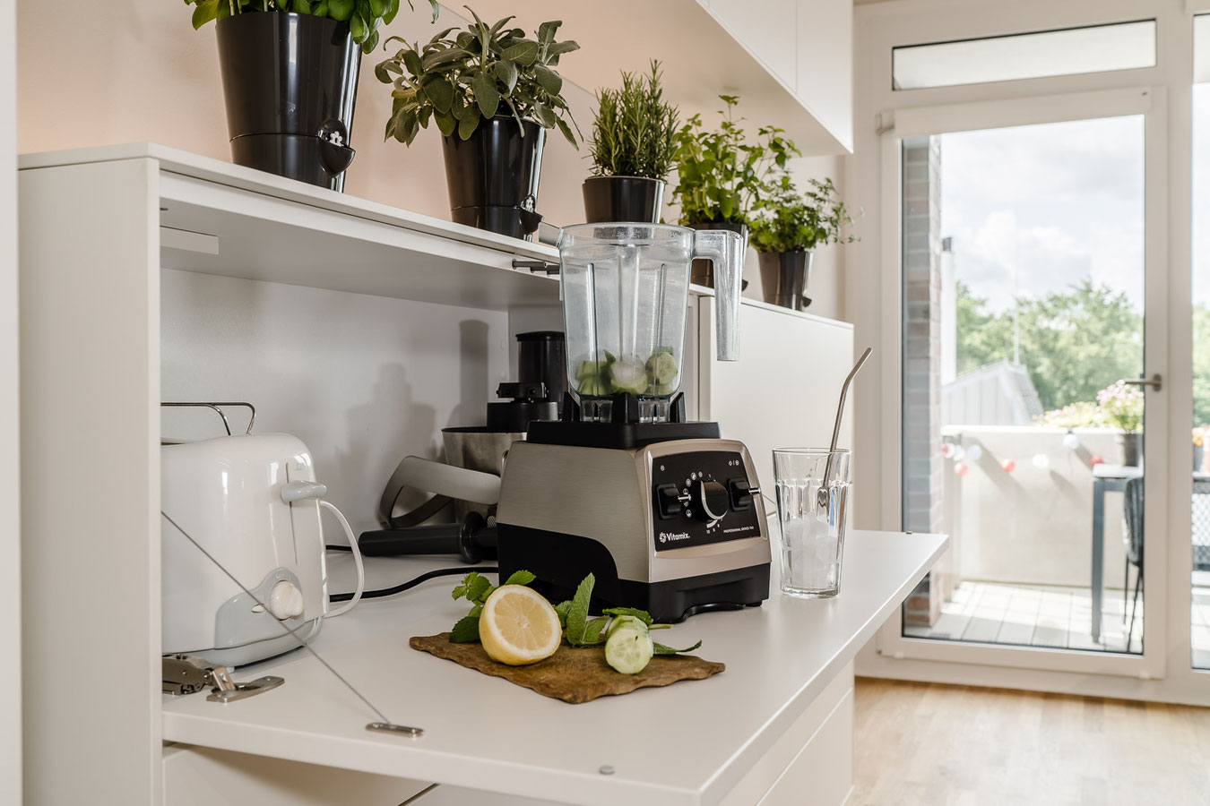 Aufgeklappte Tür, auf der eine Mixer und Zutaten für einen Sommerdink mit Zitrone, Gurke und Eis 