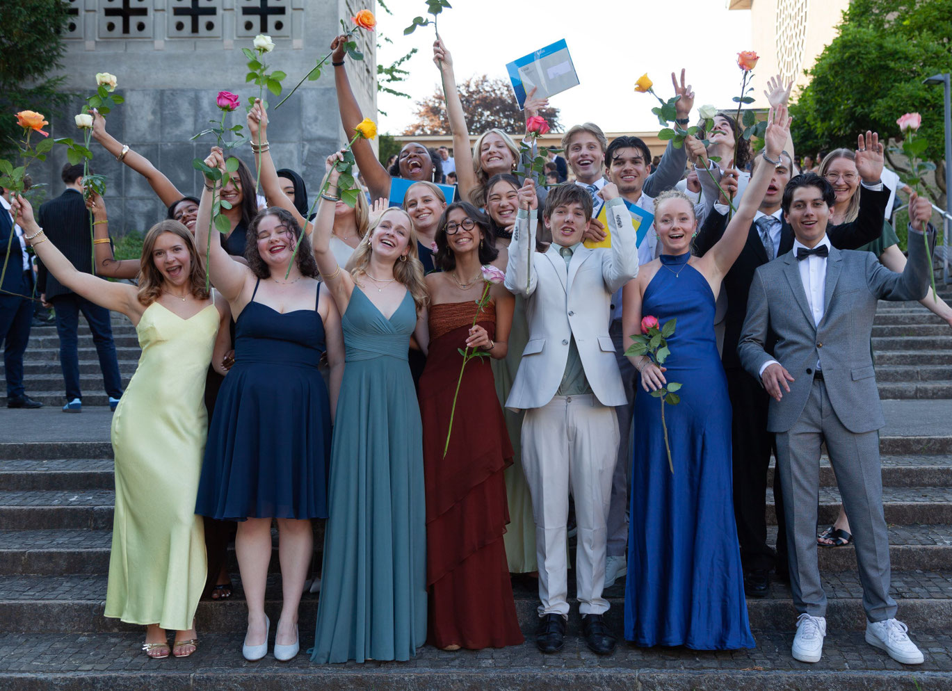 Festlich gekleidete Absolventinnen und Absolventen der Kantonsschule Musegg jubeln auf einer Treppe mit Rosen und Maturazeugnissen bei der Maturafeier 2026 in Luzern.