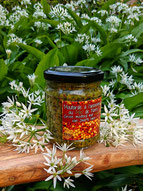 Pot de moutarde à l’ancienne au miel de noire et à l’ail des ours sur une planche en bois entouré de fleurs d'ail des ours, arrière-plan d'ail des ours en fleurs.