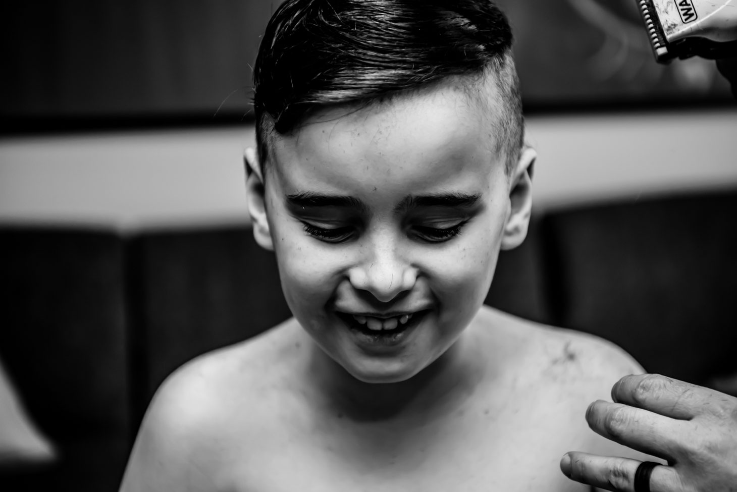 Black and white photo of mom giving child a haircut. Only mom's hands are visible. Son looks happy. 