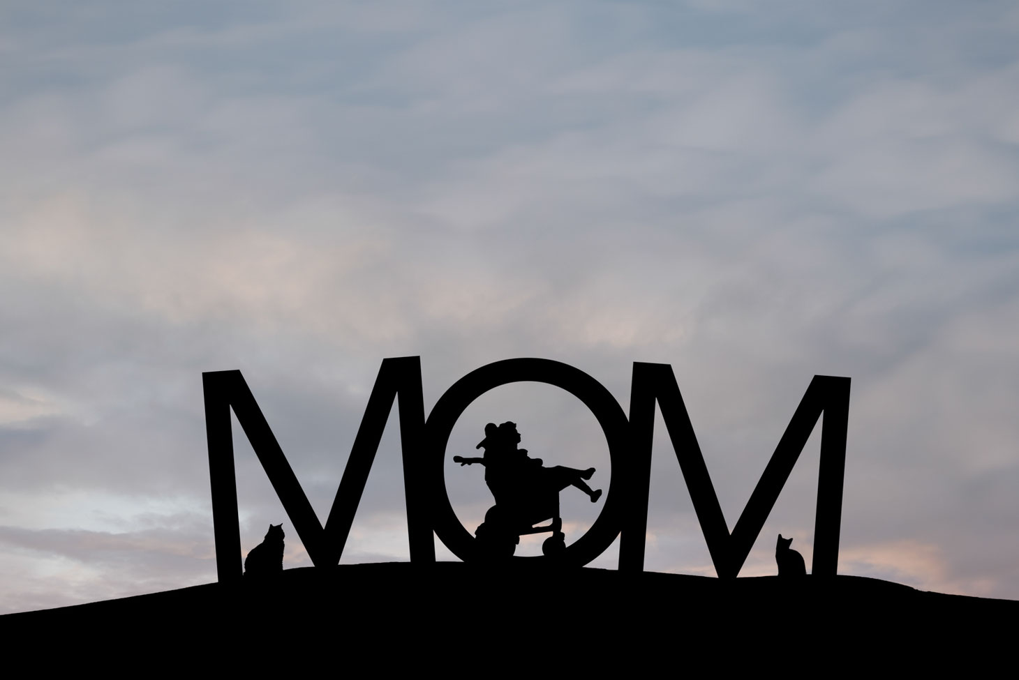 silhouettes of girl in a wheelchair and 2 cats in the letters MOM on a hill. Sky is blue, grey, and pink.