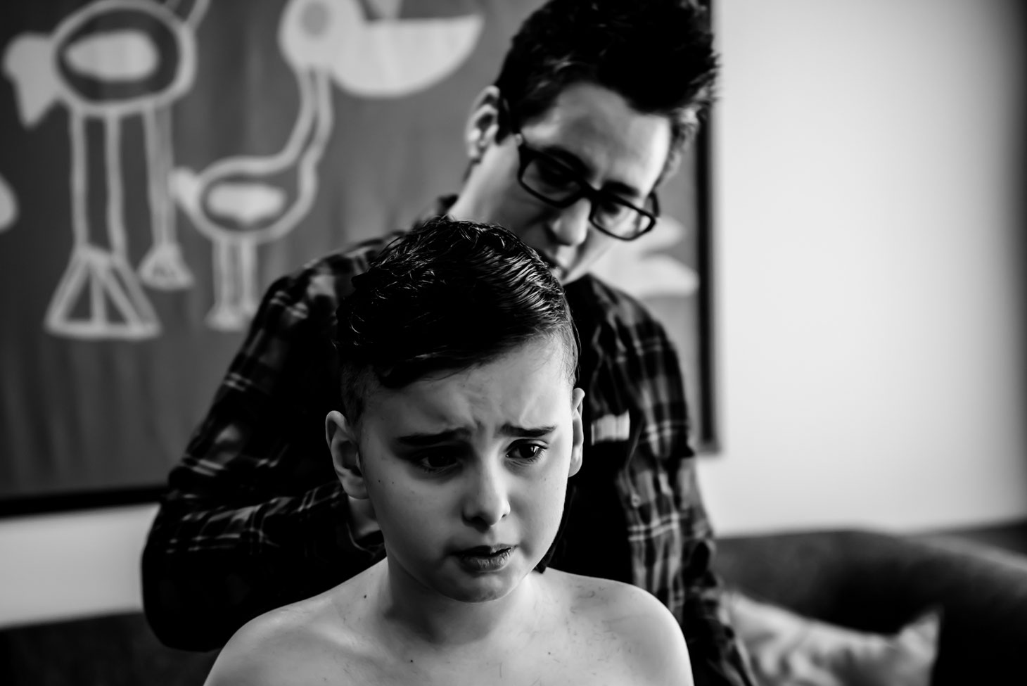 Black and white photo of mom giving child a haircut. Son looks unhappy. 