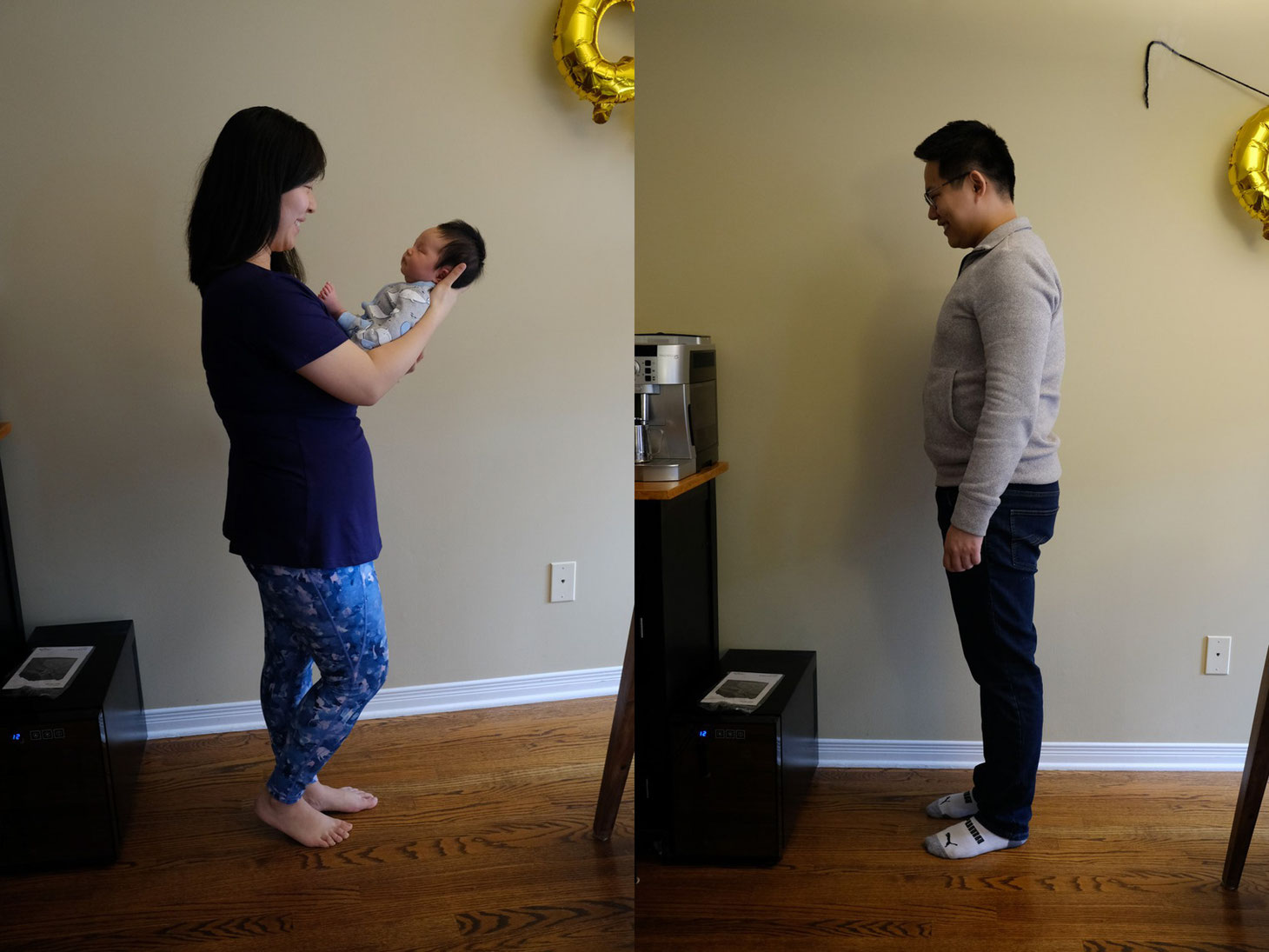 Mom holding baby wearing blue pants and blue shirt against a beige wall. Dad standing against a beige wall. 