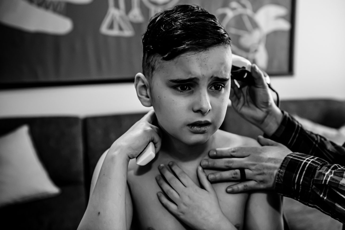 Black and white photo of mom giving child a haircut. Son looks unhappy. 