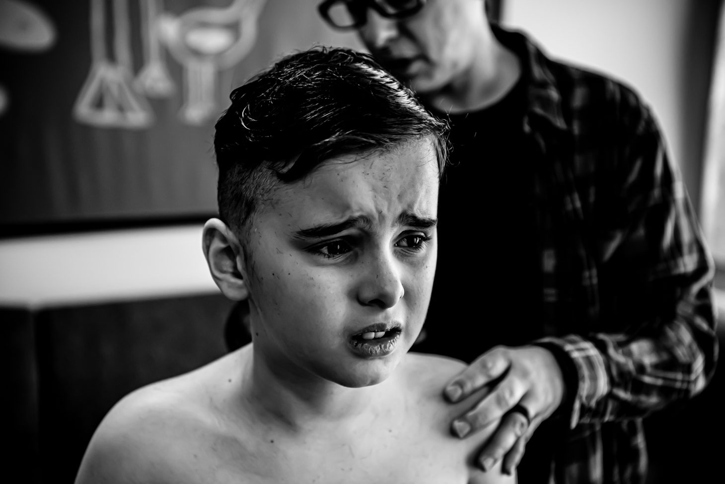 Black and white photo of mom giving child a haircut. Son looks unhappy. 