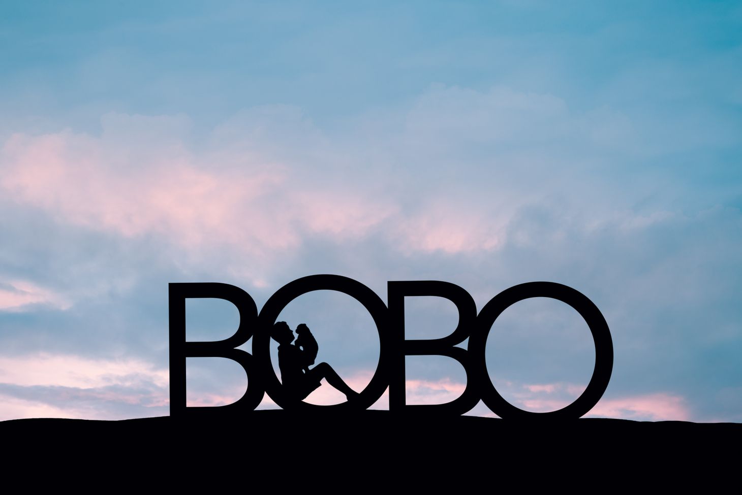 silhouette of boy and dog in the first O in the word BOBO. Sky is pink and blue. 