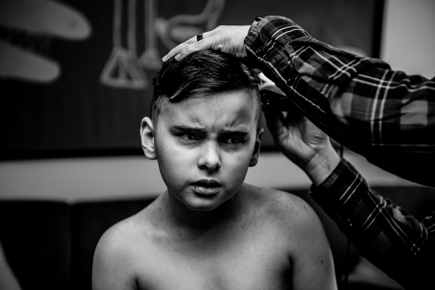 Black and white photo of mom giving child a haircut. Son looks unhappy. 