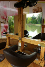 Friseurstuhl im Salon mit Blick durch den Spiegel nach draußen auf den Weiher. Das Bild zeigt den komfortablen Stuhl und die entspannende Aussicht, die unseren Kunden während ihrer Behandlung geboten wird