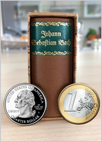 One of two tiny biographies in the Bach Shop. It is brown, about the height of three Euro coins, and comes in a brown slipcase. In the background, you can see a residential environment. At the bottom of the picture is a Euro and a US Quarter for a size co