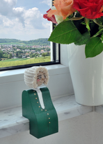 A Bach edge sitter sits on a windowsill. Behind the figure, you can see a landscape through the window; on the right is a white flowerpot with a flower.