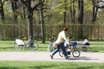 März im Schlosspark Charlottenburg. Liegender Mann auf der Parkpank und Frau, neben dem Fahrrad fahrenden Jungen laufend. Foto: Helga Karl