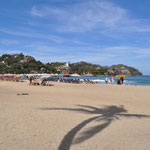 Der Strand in Sayulita - es reiht sich Sonnenschirm an Sonnenschirm. Etliche Surfbeginner sind nebeneinander im Wasser und versuchen die Wellen zu erwischen.