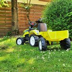 Tracteur à pédales jaune avec remorque sur la pelouse fleurie de pâquerettes, clôture en bois en arrière-plan