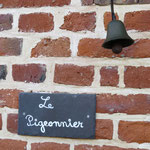 Plaque en ardoise "Le Pigeonnier" et cloche en fonte sur mur en briques rouges à joints blancs, entrée du gîte