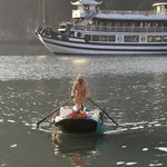 Een vrouw die rondvaart tussen de cruiseschepen op Halong Bay en haar handel aan de toeristen probeert te verkopen