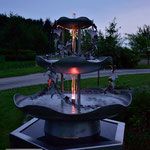 Edelstahlbrunnen -  Gartenbrunnen aus Edelstahl mit Efeuranken auf Granitsäule - LED-Beleuchtung in der Dämmerung (© Raven Metall Design)