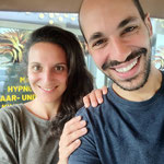 Ein Nahaufnahme-Porträt einer lächelnden Frau und eines Mannes, wobei der Mann seine Hand auf die Schulter der Frau gelegt hat.