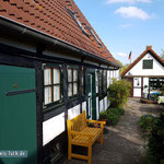 Links Seitenansicht des Ferienhauses mit Klönschnackbank im Innenhof. Das Häuschen am Bildende sieht zwar wohnlich aus, ersetzt aber nur raren Kellerraum.