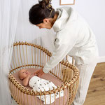 Mama beugt sich übers Baby welches im Stubenwagen liegt