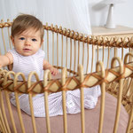 Kind sitzend im Stubenwagen aus Korb