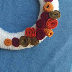 ghirlanda rivestita in lana, decorata con fiori in lana e panno, perle di legno. Diametro cm 15 circa. 