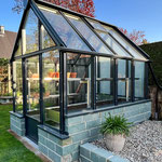 Viktorianisches Gewächshaus im Vintage-Stil, transparente Glasflächen, kunstvolle Stahlstruktur, eingebette in üppige Gartenlandschaft.