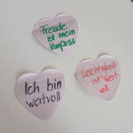 Das Bild zeigt Affirmationen, die auf Herz-förmige Post-It geschrieben sind: Z.B. "Freude ist mein Kompass"