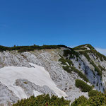 Wir würden nun das Schneefeld queren, und auf der Wiese darüber rechts entlang des Felsabgrundes weitergehen