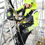 Eine Person bedient ein Rettungsgerät mit Hubfunktion, welches an einem Gerüstbauteil angeschlagen ist.