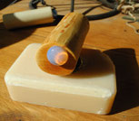 ein handgemachter Seifenhalter aus Holz, naturfarben, mit einem Schmuckstein; mit einem integrierten Magneten; platziert auf einem Stück heller Seifen