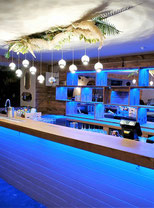 Installation d’un éclairage LED décoratif dans un bar, combinant rubans LED bleus et suspensions lumineuses pour créer une ambiance chaleureuse et moderne dans un établissement tertiaire