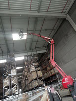 Installation d’un luminaire LED industriel en hauteur à l’aide d’une nacelle dans un entrepôt logistique avec rayonnages en activité