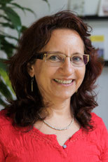 Ein Portrait von Christine Kunter-Lehner, Osteopathin und Focussing-Trainerin in der Praxis Octopus in Graz. Das Foto wurde vor einer Pflanze und einem Regal aufgenommen. Sie hat mittellange Haare mit leichten Wellen, trägt eine Brille eine rote Bluse.