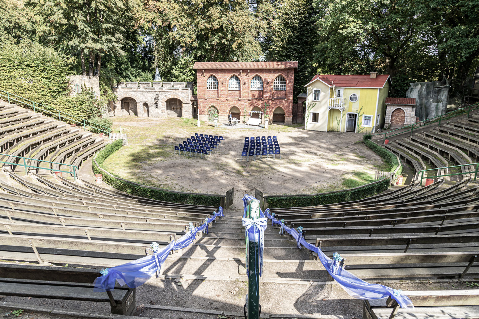 Trauung im Freilichttheater. Die Stühle für die Trauung stehen unten auf der Bühne, die Kulisse ist von einem Theaterstück. 