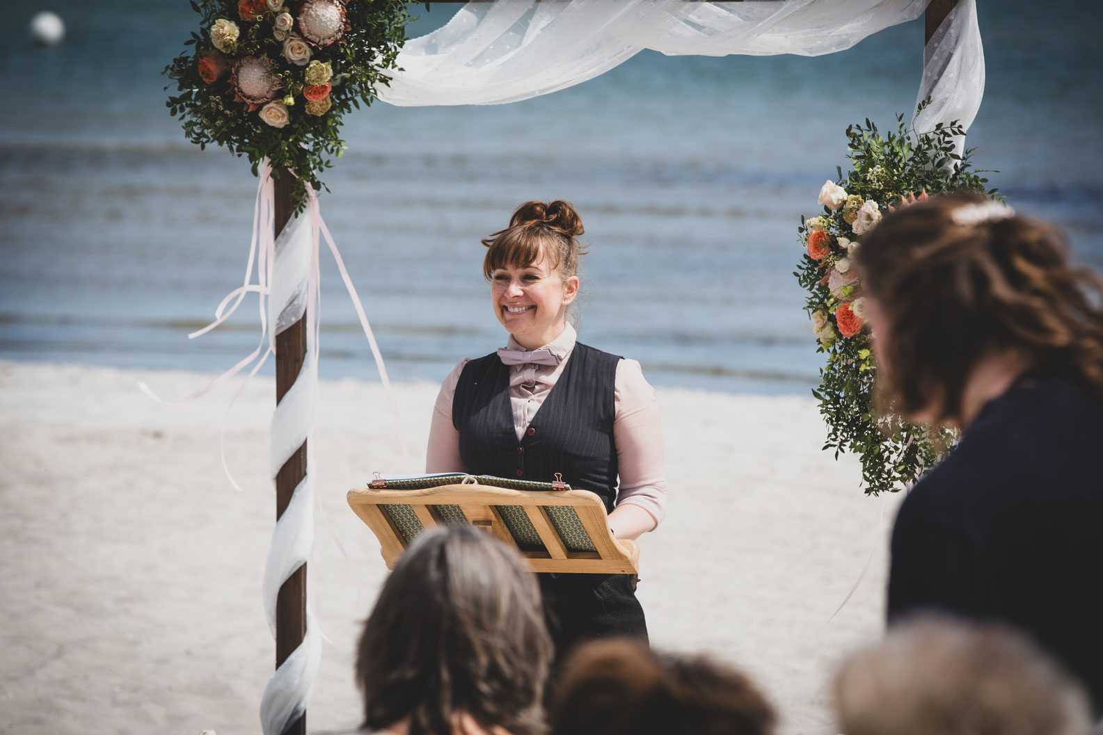Braut am Strand hält ihre Blumenkinder an den Händen, das Klein weht im Wind, hinten im Bild die Ostsee